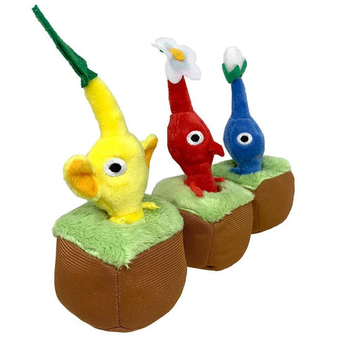 Three pikmin plush, all in a little plush grass and dirt base. The yellow pikmin has a leaf, the red pikmin has a white flower, and the blue pikmin has a white bud