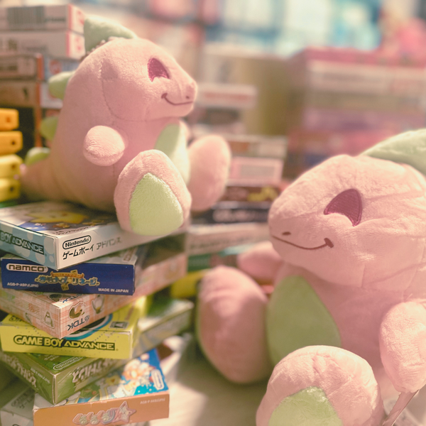 A posed photo of the two dinosaur plush sizes on stacks of retro japanese video games.