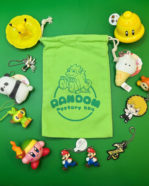 An example of the items you might find in a random mystery bag. In the middle is the green bag. It’s surrounded by items: a pikachu figurine, a dragon quest metal charm, a small soft panda keychain, a keychain of the Pokemon grookey, a Kirby figure holding a flaming sword, a keychain of two Mario’s running, a Zelda breath of the wild logo keychain, a rubber keychain of an anime character from Chainsaw Man, a waddle Dee figure, a small soft ice cream cone keychain, and a plastic Mario bell keychain