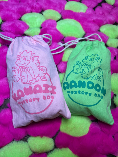 Image of two mystery bags. Kawaii mystery bag on the left is pink, featuring a Pink Gorilla logo. Random mystery bag on the right is green, featuring a pink gorilla logo.