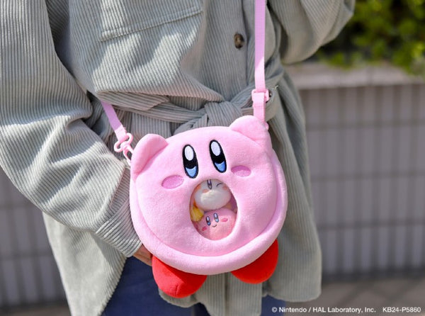 A promotional image from Nintendo/HAL Laboratory of the Kirby plush bag being worn. The photo is a close up and only the person's jacket and arm can be seen. The bag is holding several little kirby plushies that can be seen through the clear window.