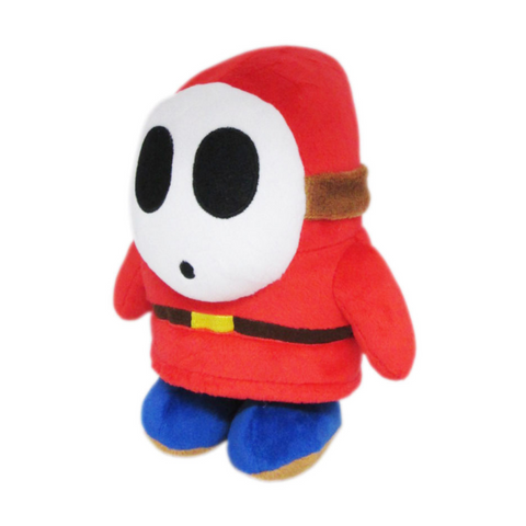 A shy guy plush. He is wearing a red hood with a white mask and blue shoes.