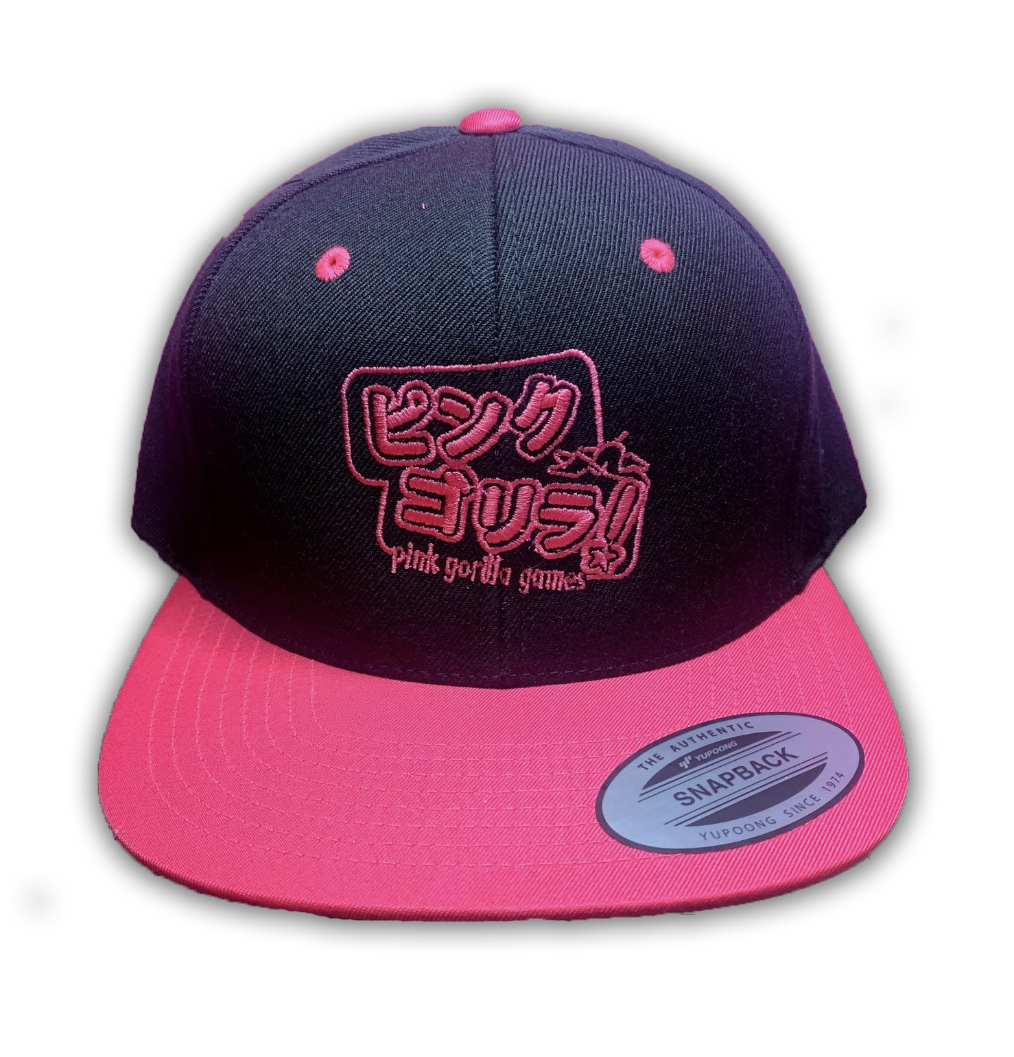 A front view of our snapback hat. The hat is black with a bright pink bill and accents. The embroidery is Japanese characters that read "Pink Gorilla", with english text that says "Pink Gorilla Games" underneath, in bright pink thread.