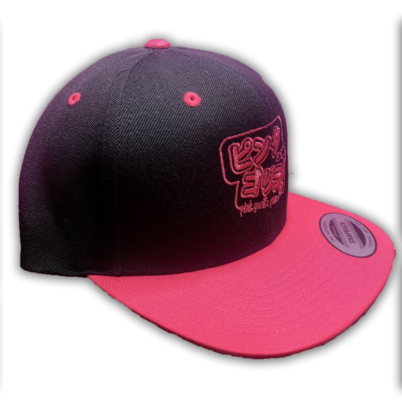 A side view of our snapback hat. The hat is black with a bright pink bill and accents. The embroidery is Japanese characters that read "Pink Gorilla", with english text that says "Pink Gorilla Games" underneath, in bright pink thread.